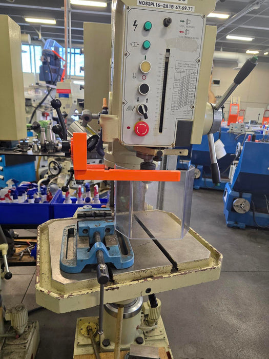 Industrial drill press with safety guarding in a workshop setting with control panel and various components.